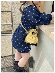 Detail of a child yellow ruched cloud bag with a gold chain strap on a navy heart dress