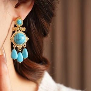 Detail of vintage gold earrings with turquoise water-drop stones on a female model