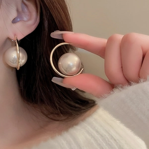 Detail of C-shaped golden hoop earrings with large faux pearl on model's earlobe