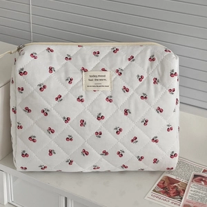 Close-up of white quilted cosmetic bag with cherry patterns and central fabric label