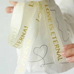 Close-up of beige fabric ribbon with gold Love Is Eternal text for romantic gift wrapping