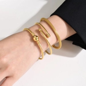 Close-up of three gold stainless steel bracelets including mesh and twisted styles on a wrist