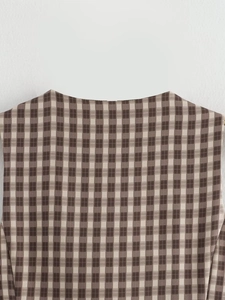 Dettaglio dello scollo rotondo e della spalla su un gilet e gonna a quadri marrone beige