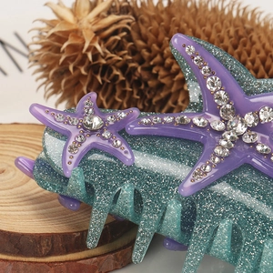 Detailed close-up of a sparkling teal hair claw clip featuring rhinestoned purple starfish