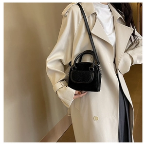 Detail shot of black plush patchwork handbag with detachable strap on beige coat