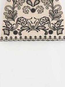 Detail of floral embroidery and black sequins on beige cotton mini skirt set fabric