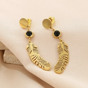 Détail de boucles d'oreilles plume dorées avec gemme noire sur fond de tissu texturé