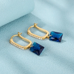 Detail of gold U-shaped earrings with blue rectangular stones and white accents