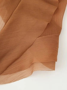 Détail de la texture du tissu plissé marron cuivré avec des plis sur une robe légère