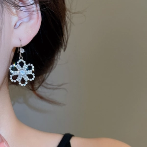 Close-up of silver hollow flower earrings with sparkling rhinestones on model ear