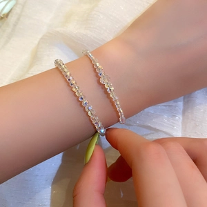 Dettaglio di due bracciali di perline con cristalli iridescenti su tessuto bianco
