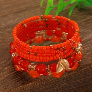 Dettaglio del bracciale boho con perline arancioni e ciondolo a foglia dorata