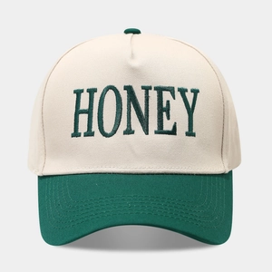 Gros plan détaillé de la broderie HONEY verte sur une casquette trucker bicolore en coton