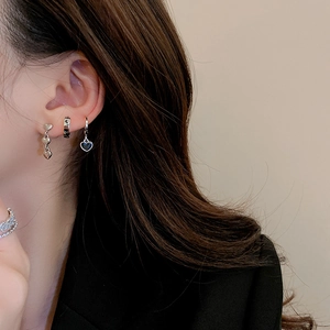 Detail view of silver heart earrings and black heart pendant hoops worn on ear