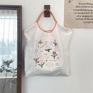 Detail of embroidered tote bag with tulip patterns and woven rope handles on a hook