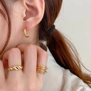 Close-up of gold-plated oval earrings and twisted rings worn by a model in a minimal style