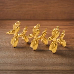 Three golden 3D balloon dog pendants on dark wood background with top hanging rings