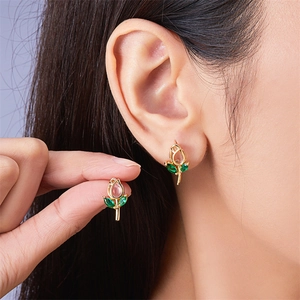 Detail of gold tulip earrings with pink gemstones and green leaves on a model