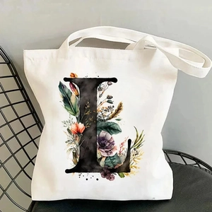 Detail view of white canvas tote bag with floral letter L print on a black chair
