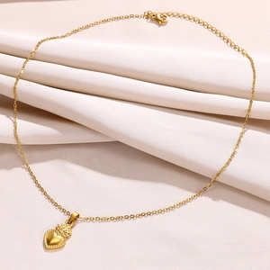 Detailed view of a vintage 18k gold heart pendant with textured edges on a beige fabric