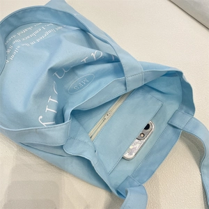 Close-up of light blue canvas tote bag showing interior zipper pocket with a phone