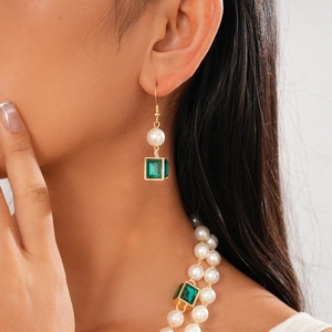 Close-up of pearl necklace with green square gems and gold earrings on female model