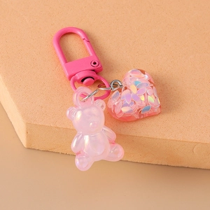 Macro detail of a pink pearlescent bear and resin heart charm on a metal lobster clasp