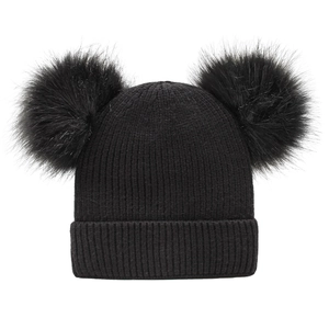 Close-up of black ribbed knit winter hat featuring two large faux fur pom-poms on top