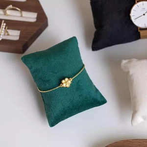 Close-up of golden floral bracelet on a dark green velvet display cushion stand