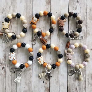 Silicone beaded keychain bracelets with animal charms and tassels on wood background