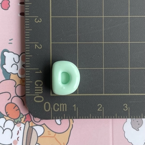 Close-up of a 1cm mini mint green resin letter D pendant on a measurement scale