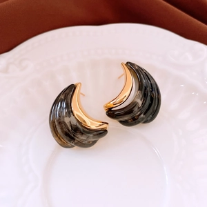 Macro detail of gold-plated crescent earrings with dark marbled resin inlays