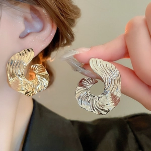 Close-up of golden fan-shaped textured earrings worn with elegant spiral metal design
