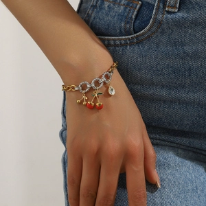 Close-up of gold and silver chain bracelet featuring red cherry and crystal pendants