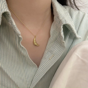 Close-up of golden croissant pendant necklace on a blue and white striped shirt