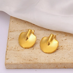 Macro detail of golden irregular fan-shaped stainless steel earrings on beige stone texture
