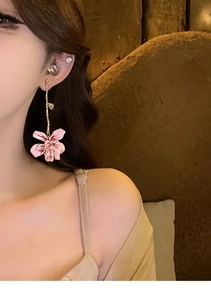 Detail of pink flower drop earrings with enamel finish worn by a model in warm light