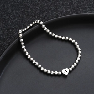 Macro detail of silver beaded heart bracelet with engraved letter A on black tray