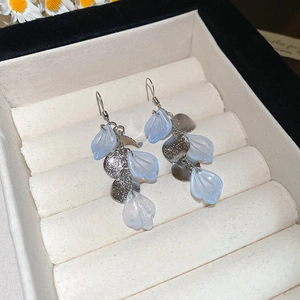 Detailed view of silver long fringe earrings with light blue petal pendants on velvet box