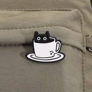 Macro detail of cartoon black cat in white coffee cup enamel pin on green canvas fabric