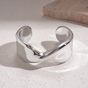Macro detail of silver wavy metal bangle with polished mirror finish on stone background