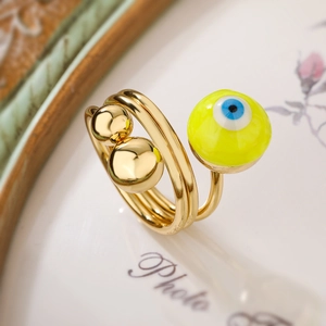 Gold-plated spiral ring with green evil eye and gold beads on a decorative background