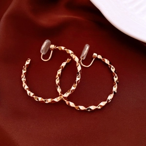 Detailed view of geometric gold earrings with diamond-cut texture on red silk background