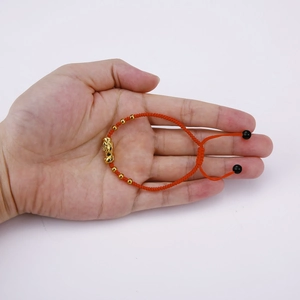 Detail of handmade red woven bracelet featuring golden Pixiu and black bead accents