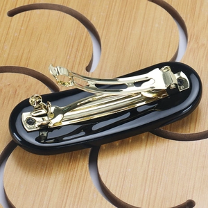 Close-up of golden metal spring clip mechanism on back of black oval hair clip