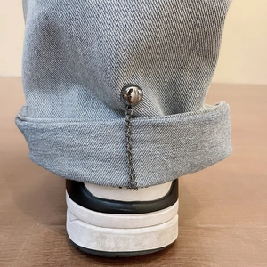 Detail of silver magnetic chain buckle and metal ball bead on light blue denim jeans hem
