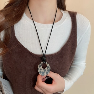 Detail of a brown resin donut pendant on a black cord necklace worn by a model