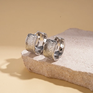 Macro shot of silver textured hoop earrings with irregular ripples on porous stone