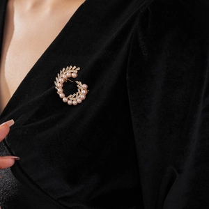 Macro detail of a C-shaped gold-plated brooch with pearls and baguette-cut zircons