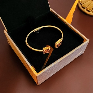 Top-down view of a golden open bangle with square hollow design in a black gift box